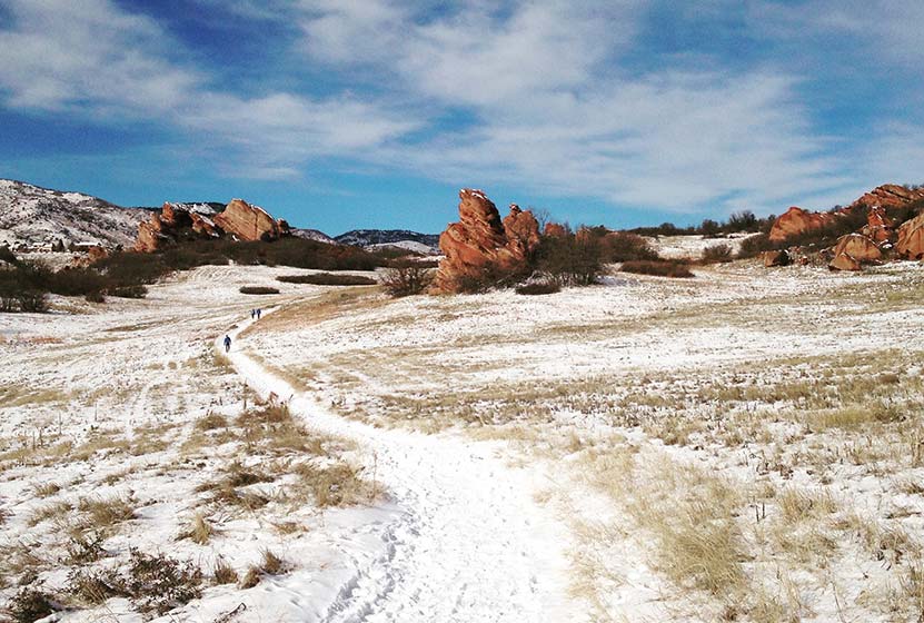 snow on trail with red rocks and blue skies at south valley park in Littleton Colorado winter hike near denver