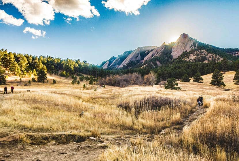 flatiron mountain formation in boulder colorado with golden meadow and hikers on trails with sunset behind mountains