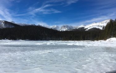 frozen brainard lake with snowcapped mountains in background on hike along waldrop trail to cmc cabin